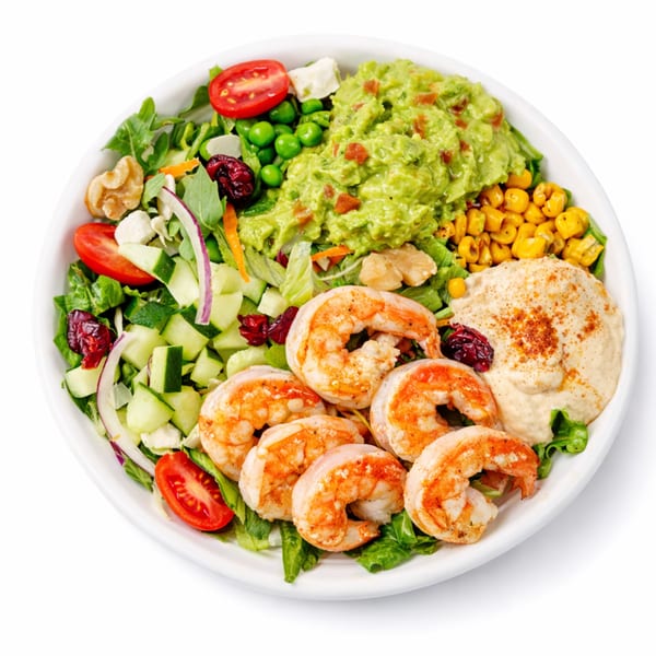 A vibrant shrimp salad bowl with guacamole, corn, hummus, and fresh vegetables.