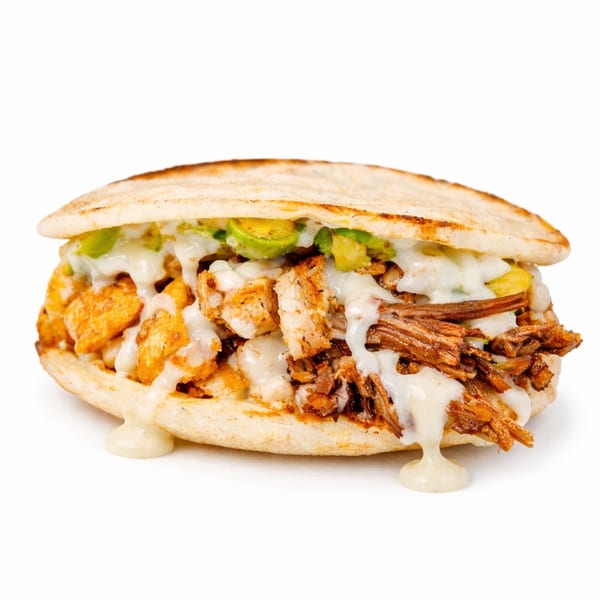 Arepa stuffed with shredded beef, chicken, avocado, and creamy white sauce, on a white background.