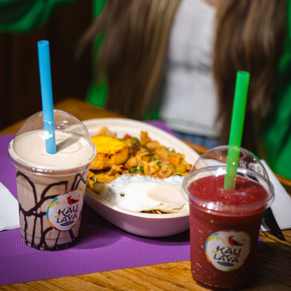 Two Kau Laya branded drinks, one chocolate and one berry, next to a Latin-American dish with eggs.