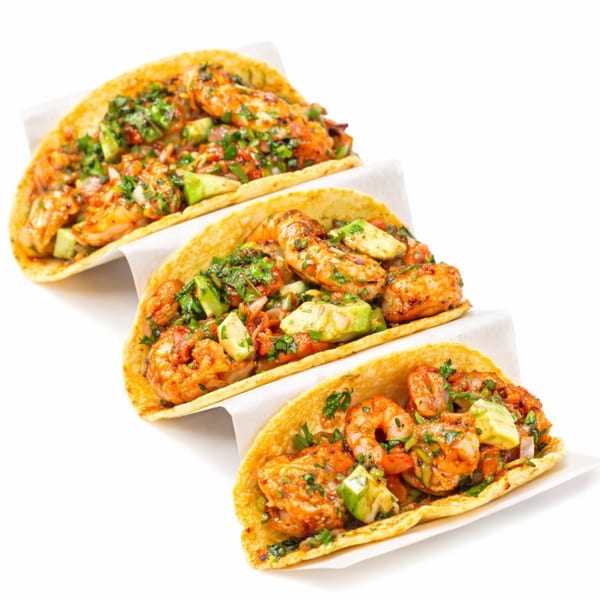 Three shrimp tacos with avocado, cilantro, and red sauce on white paper, against a white background.