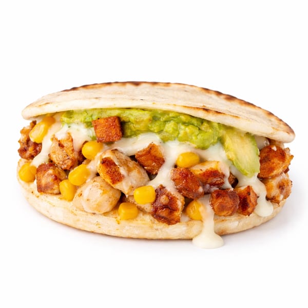 Arepa filled with grilled chicken, corn, melted cheese, and guacamole, on a white background.